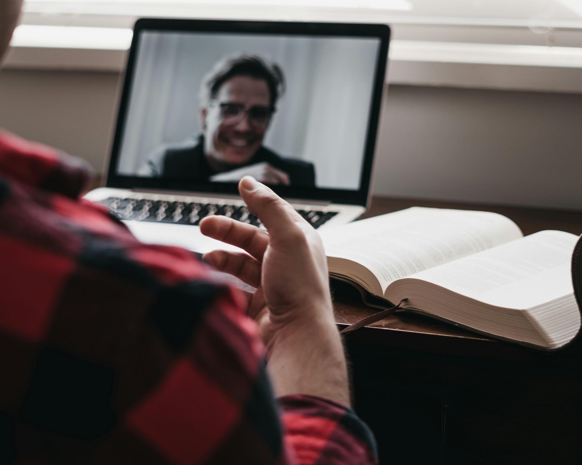A pastor on a video call in a mentoring conversation, Bible open on the desk