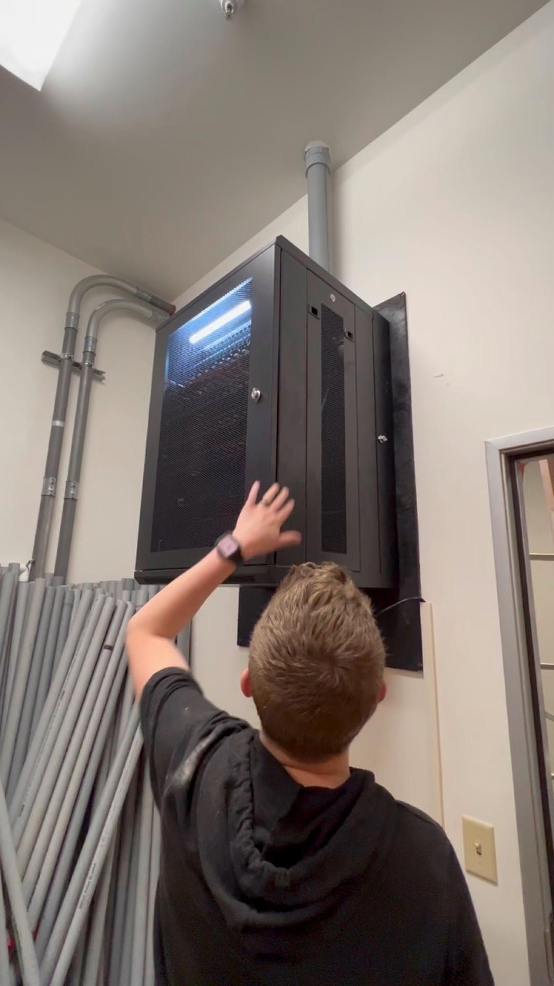 A FinWell technician reaching into a wall-mounted server cabinet during a service call