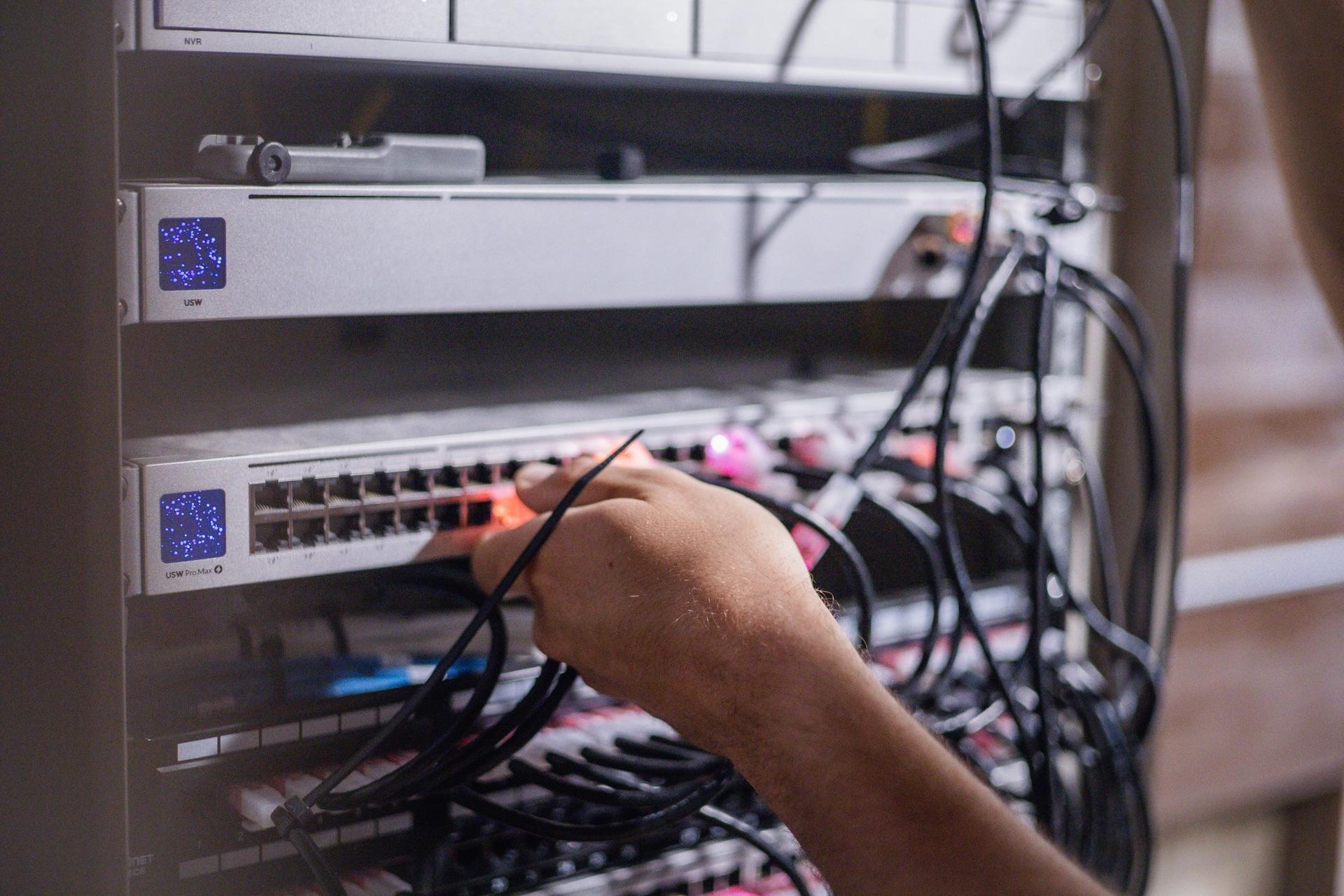 A FinWell technician plugging a cable into a network switch, with a colleague working nearby